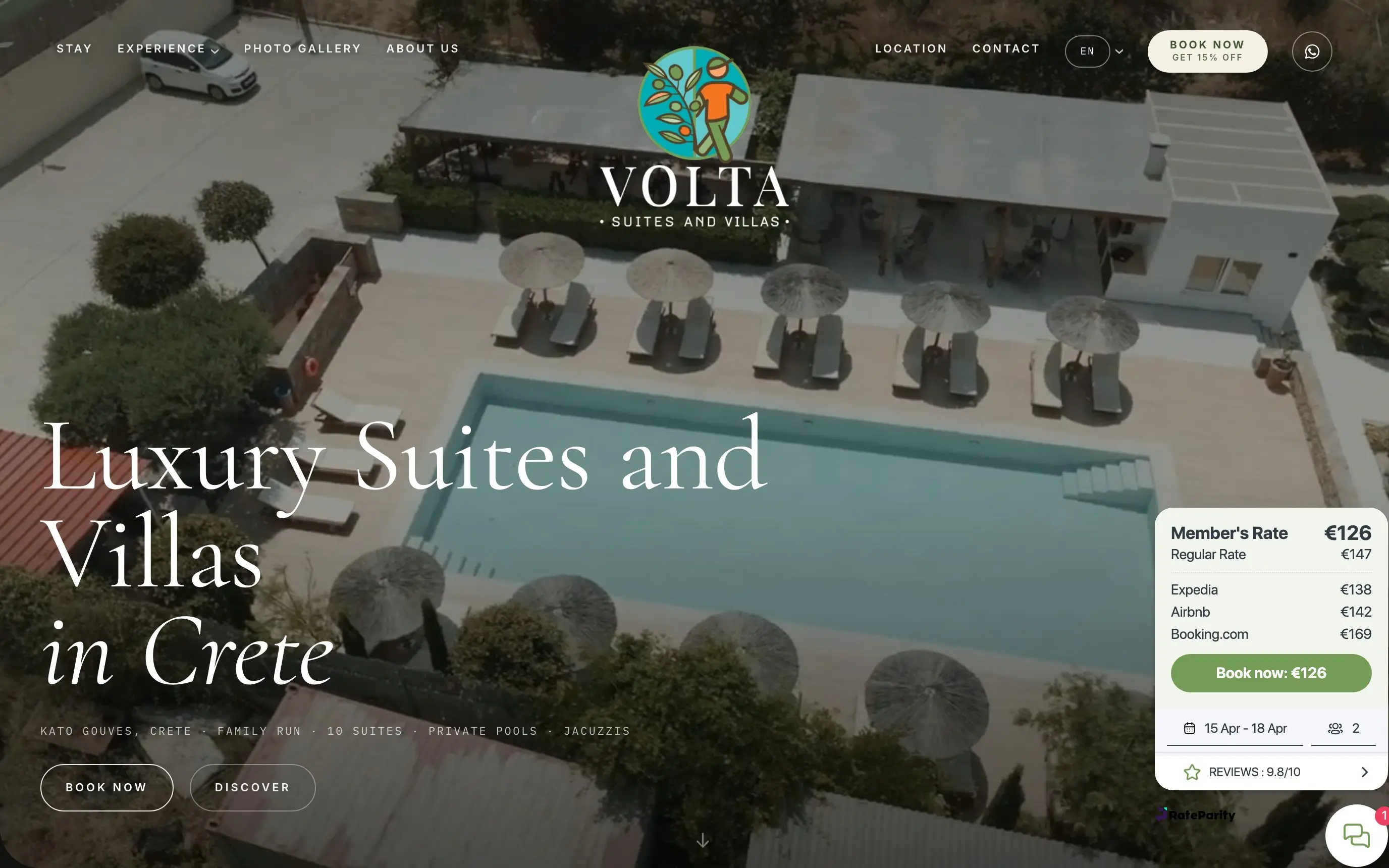 The voltastay.com homepage on a laptop: a pool with sun loungers seen from above, the headline «Luxury Suites and Villas in Crete» and a booking box showing the member rate next to the platforms' prices